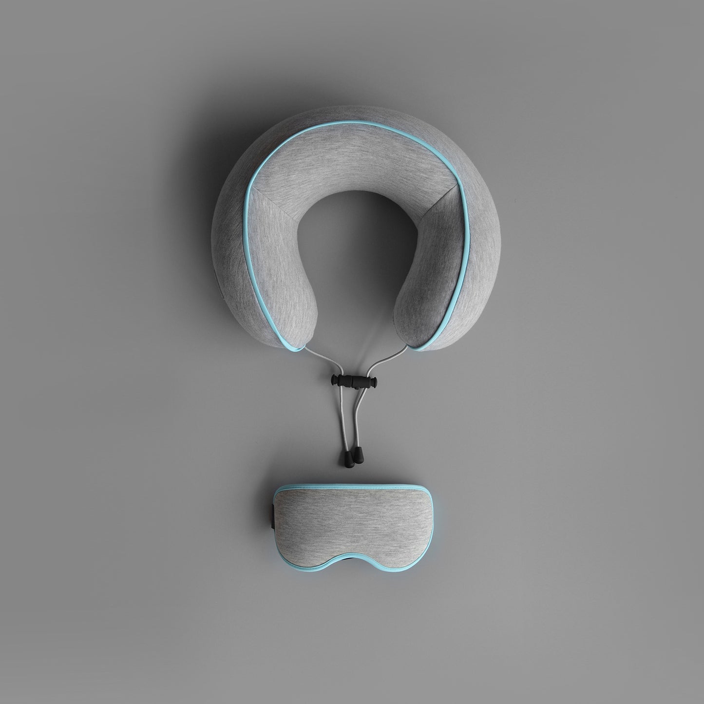 Gray neck pillow and eye mask set on a gray background